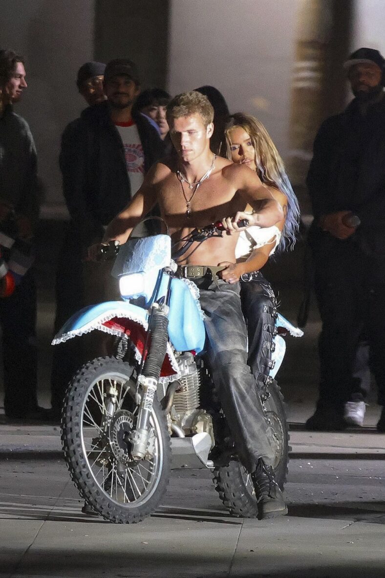 Karol G on a motorcycle with a shirtless male model