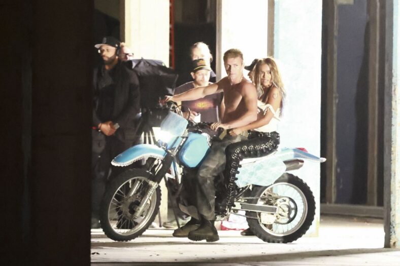 Karol G on a motorcycle with a shirtless male model